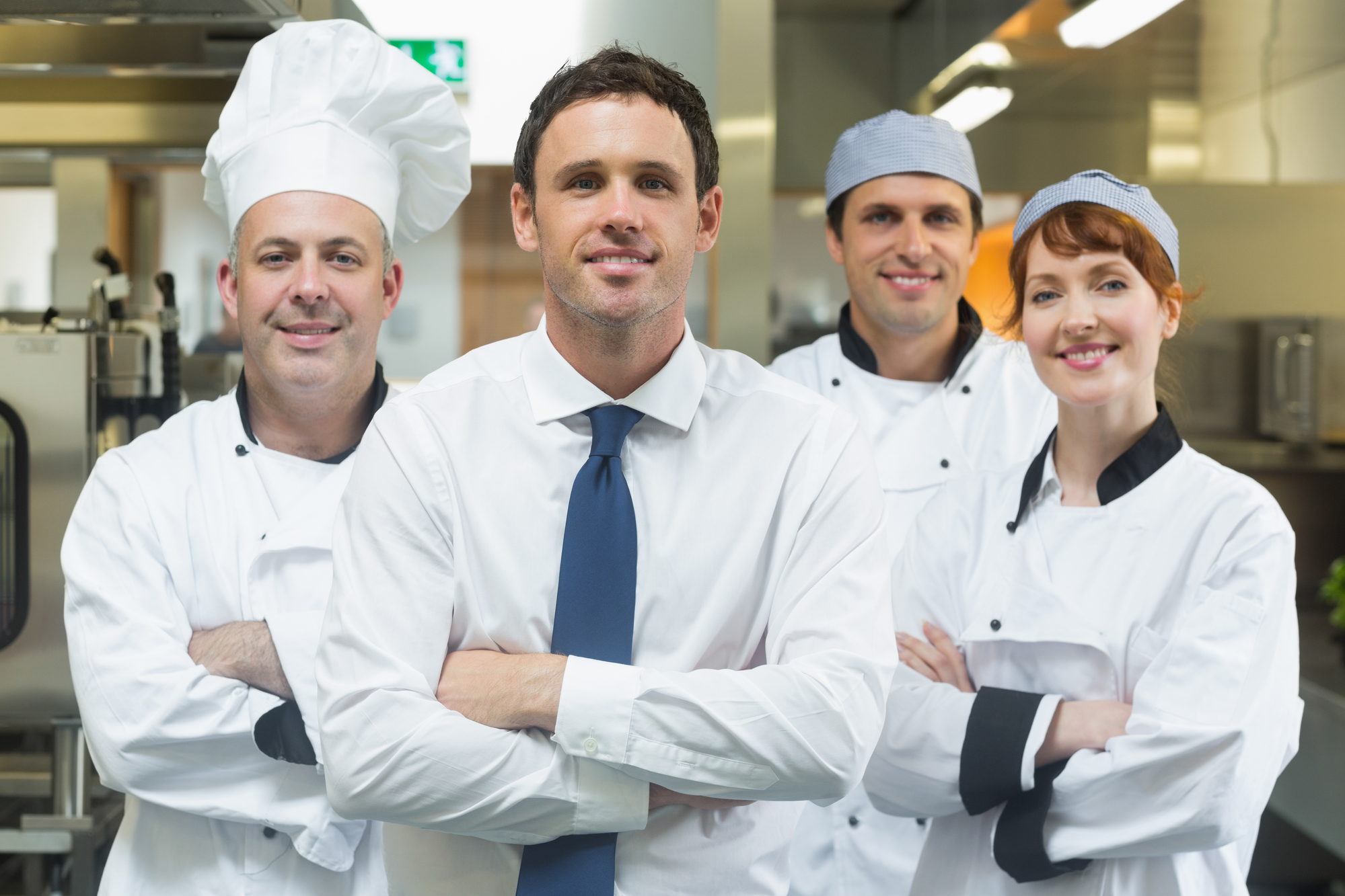  A restaurant supervisor stands with crossed arms in front of three smiling chefs.
